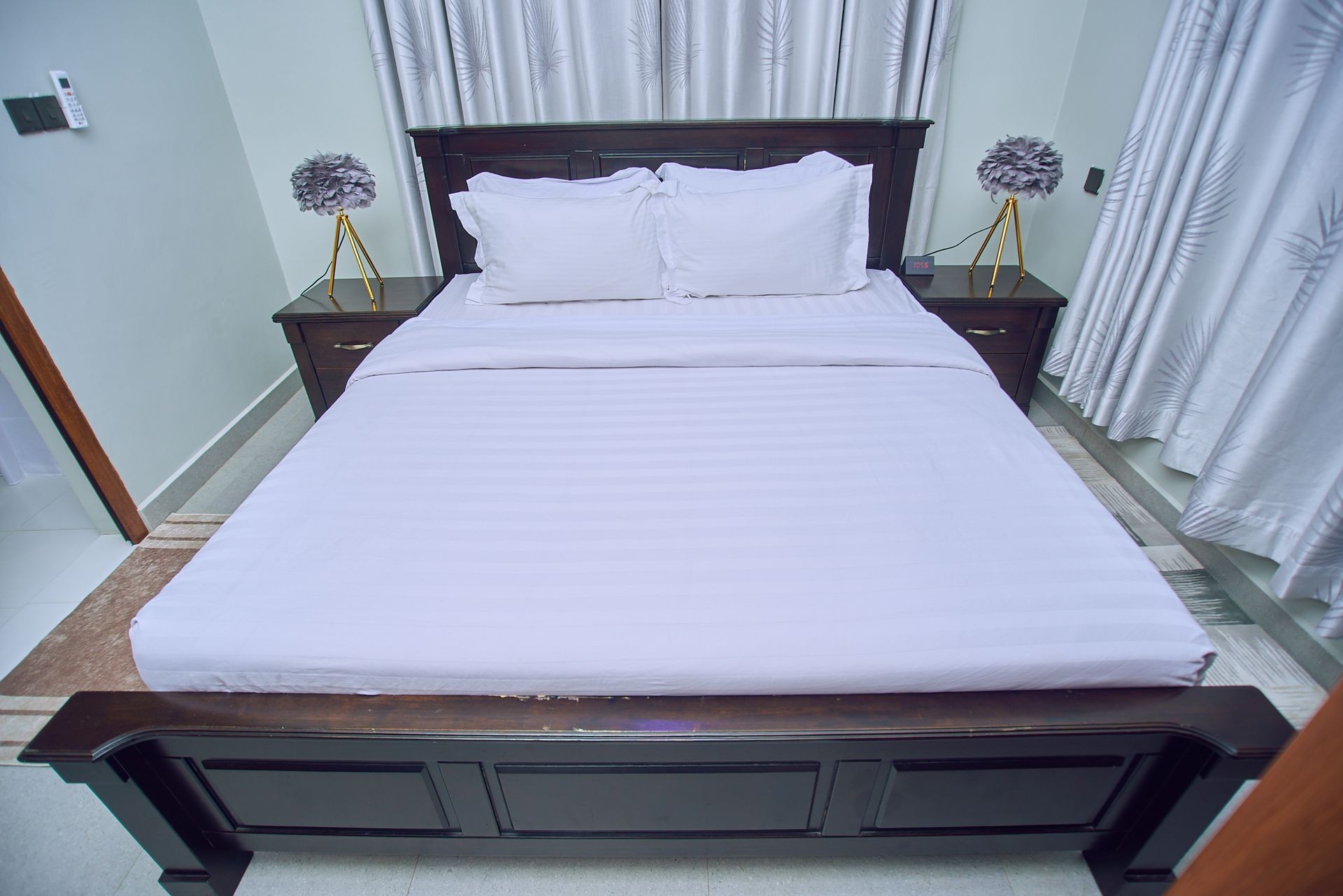 Neatly made bed with white linens, flanked by dark wooden nightstands and decorative lamps.